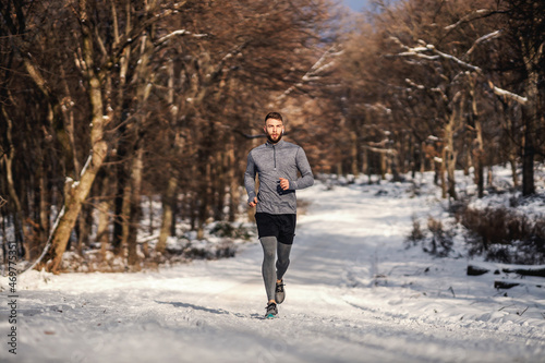 Sportsman running on snowy path in woods at winter. Winter sport, healthy habits, outdoor fitness