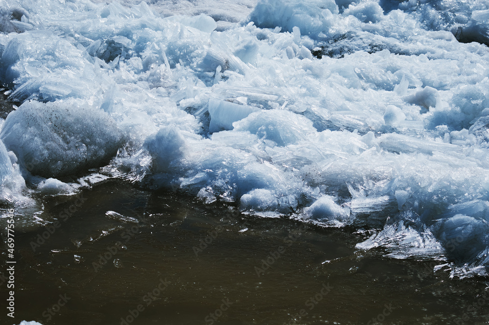 Texture of ice on a spring day under the sun. Puddle and glare from the sun. Amur river. Ice needles.