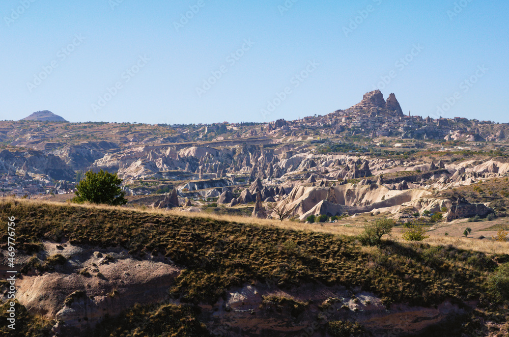 Beautiful panoramic landscape photo of typical geologic formations of Cappadocia. Amazing shaped sandstone rocks. Ancient Uchisar in the horizon. Famous touristic place and romantic travel destination