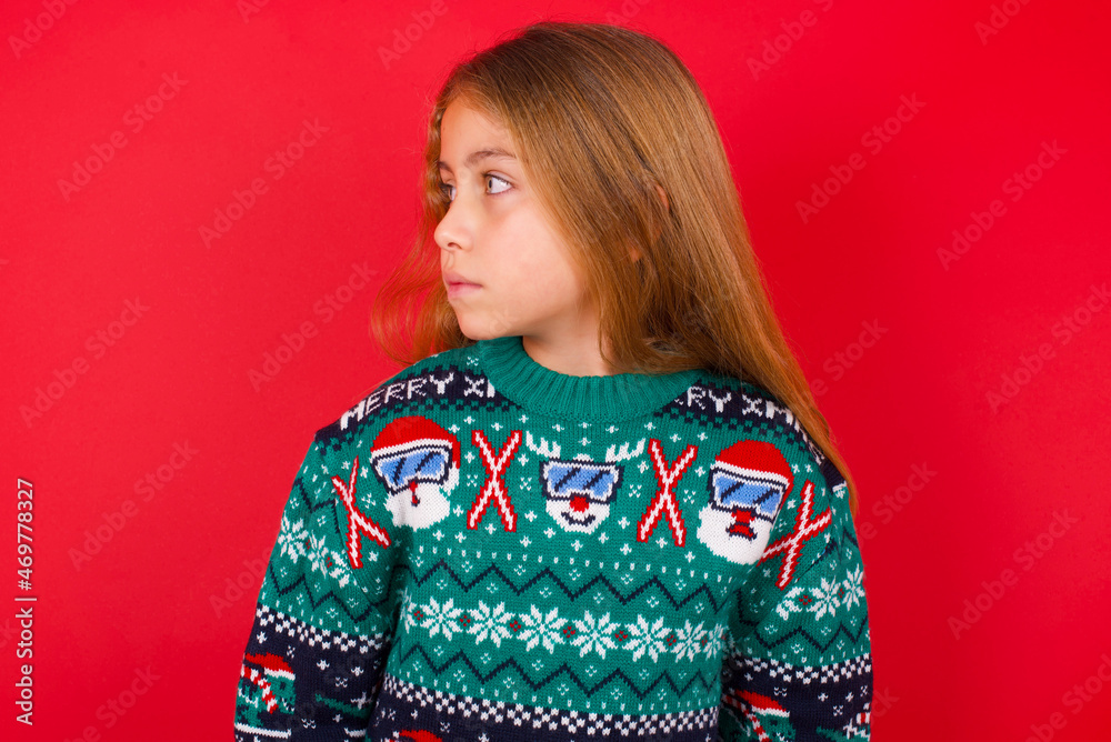 Side view of young happy smiling little kid girl wearing knitted sweater christmas over red background Side view of young happy smiling little kid girl wearing knitted sweater christmas over red background