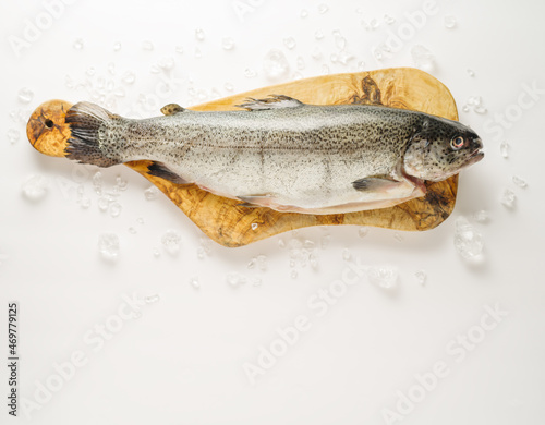 Pieces of ice are scattered on a white background. One fresh fish on a cutting board. There are no people in the photo. Minimalism. Pastel shades. Restaurant, hotel, cafe, home cooking.