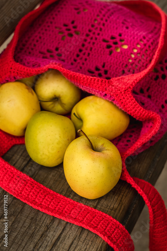 Golden apples in a red net bag on a wooden bench. Zero waste concept.