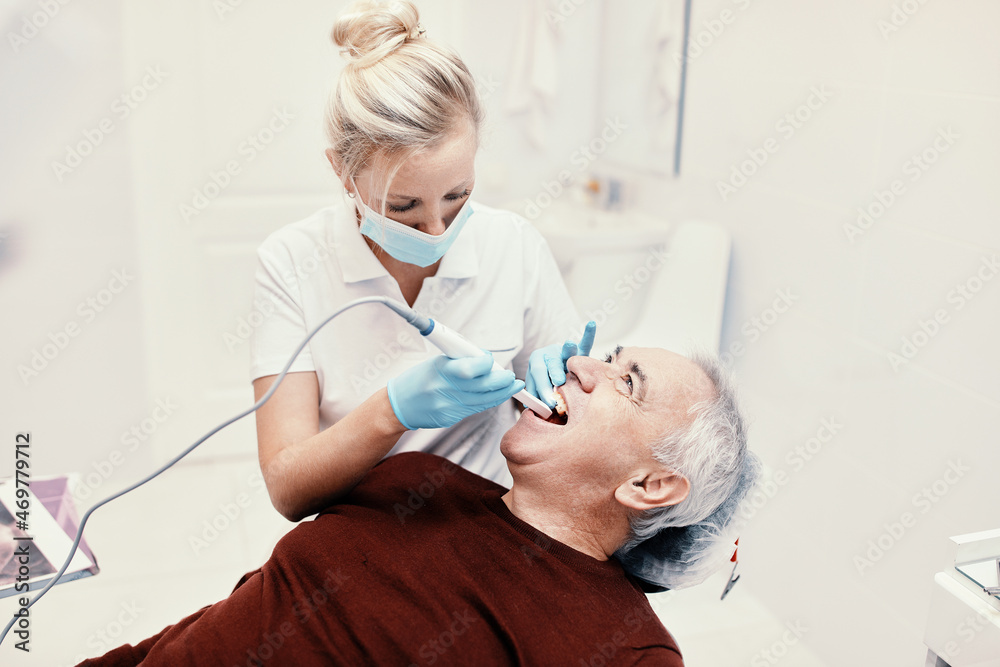 Fototapeta premium Woman doctor dentist works with an elderly man in a dental chair treats teeth and shows x-rays