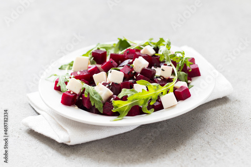 Salad with beetroot, cottage cheese, arugula and white and black sesame seeds on a plate on a linen napkin on a light gray background