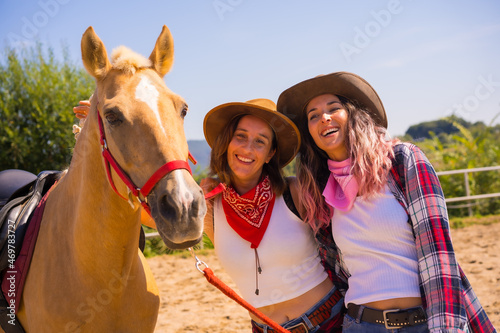 Posing of two cowgirl women next to a horse on a horse riding, with South American outfits