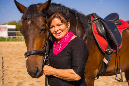 Portrait of an adult woman on a horse stroking a brown horse, dressed in South American outfits