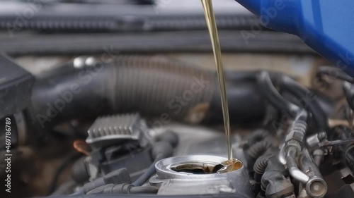hand in a white glove opens the filler cap of a car engine and pours fresh engine oil from a blue canister.