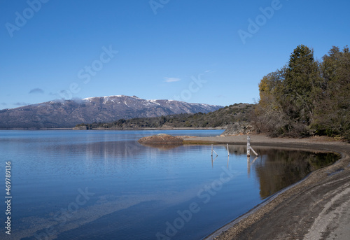 View of the lake shore, beach, forest and blue water lake in a summer sunny day. The alps and mountains in the background.