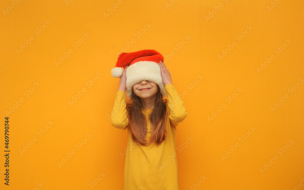 Emotional cute little girl in santa hat on yellow background with a copy space. Emotional cute little girl in santa hat on yellow background with a copy space.