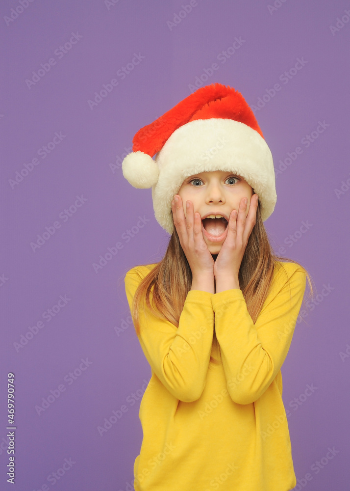 Emotional cute little girl in santa hat on violet background with a copy space. Emotional cute little girl in santa hat on violet background with a copy space.
