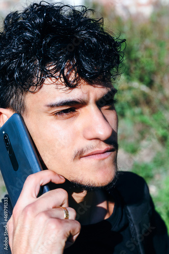 Portrait of young man talking on his smartphone. Outdoor image of a young man with curly hair speaking on a cellphone.