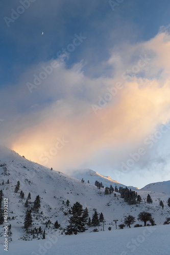 Winter calm cloudy mountain landscape at sunset. Splendid snow-covered mountains view with beautiful fir trees on slope.