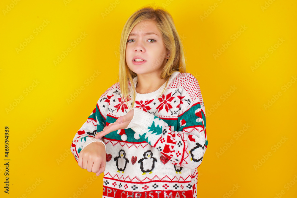 caucasian little kid girl wearing knitted sweater christmas over yellow background In hurry pointing to watch time, impatience, upset and angry for deadline delay.