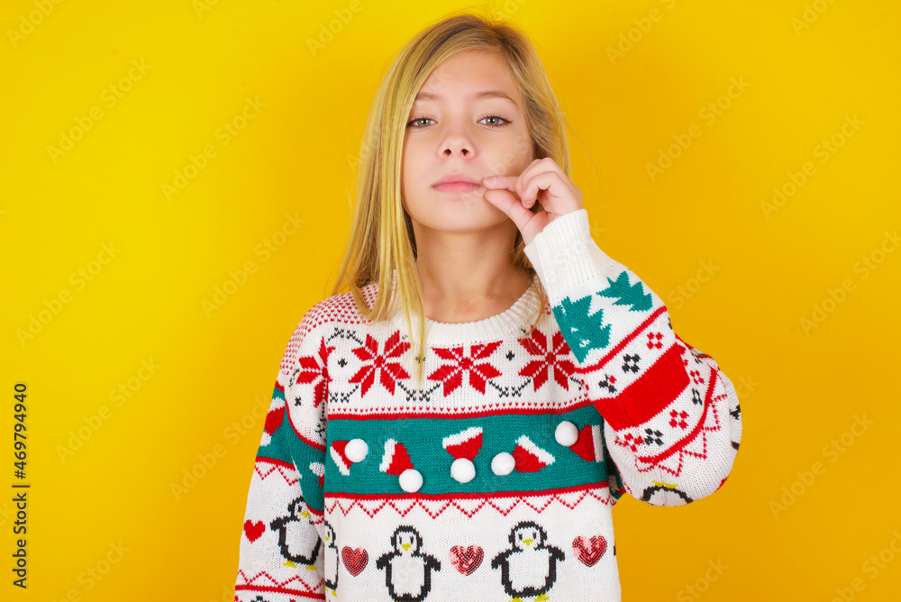 caucasian little kid girl wearing knitted sweater christmas over yellow background mouth and lips shut as zip with fingers. Secret and silent, taboo talking. caucasian little kid girl wearing knitted sweater christmas over yellow background mouth and lips shut as zip with fingers. Secret and silent, taboo talking.