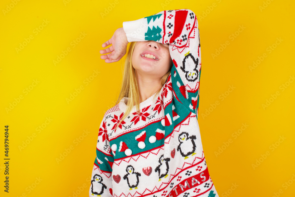 caucasian little kid girl wearing knitted sweater christmas over yellow background covering eyes with arm smiling cheerful and funny. Blind concept. caucasian little kid girl wearing knitted sweater christmas over yellow background covering eyes with arm smiling cheerful and funny. Blind concept.