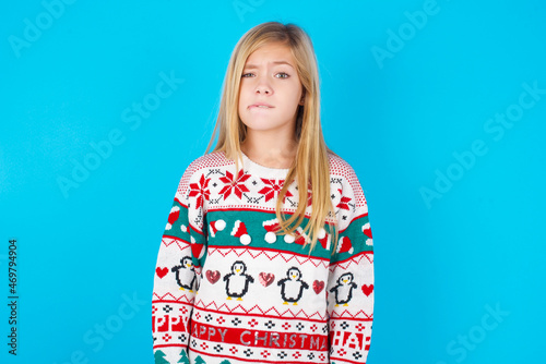 caucasian little kid girl wearing knitted sweater christmas over blue background being nervous and scared biting lips looking camera with impatient expression, pensive. © Roquillo