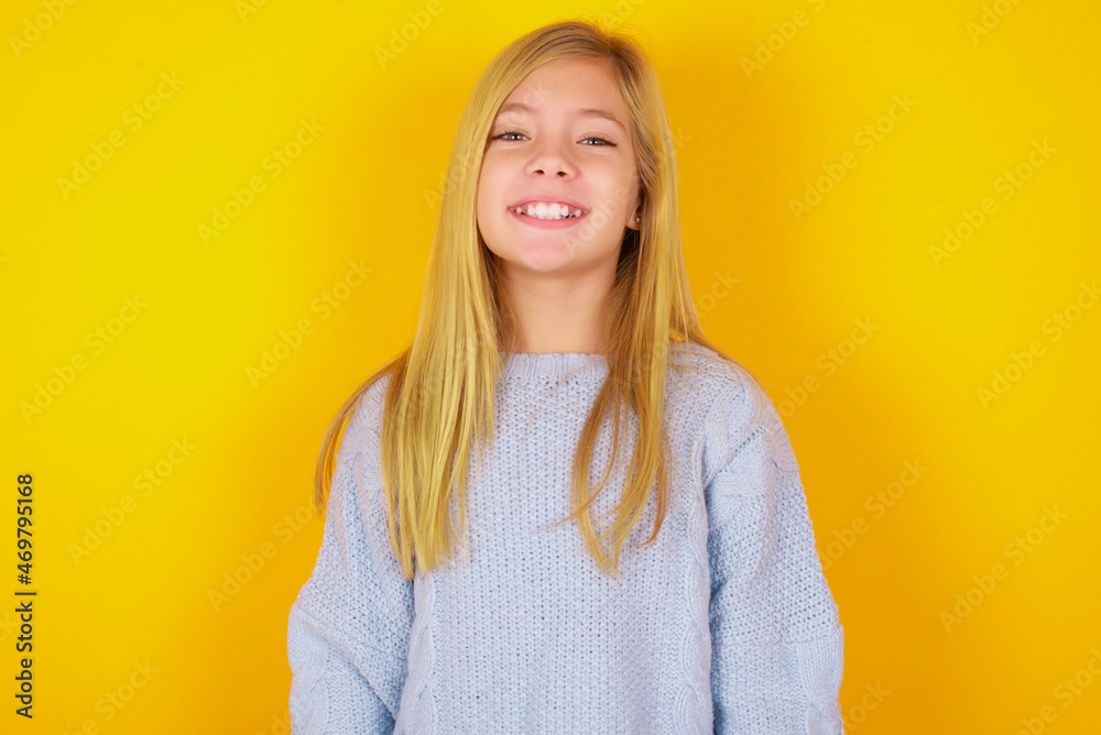 caucasian kid girl wearing blue knitted sweater over yellow background with a happy and cool smile on face. Lucky person. caucasian kid girl wearing blue knitted sweater over yellow background with a happy and cool smile on face. Lucky person.