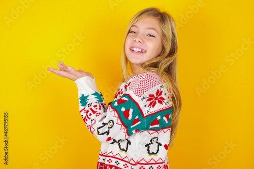 caucasian little kid girl wearing knitted sweater christmas over yellow background pointing aside with hands open palms showing copy space, presenting advertisement smiling excited happy © Roquillo