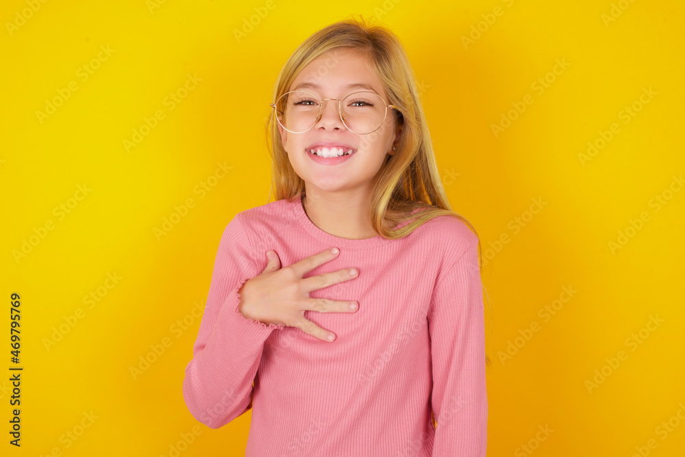 caucasian little kid girl wearing long sleeve shirt over yellow background smiles toothily cannot believe eyes expresses good emotions and surprisement
