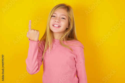 caucasian little kid girl wearing long sleeve shirt over yellow background smiling and looking friendly  showing number one or first with hand forward  counting down