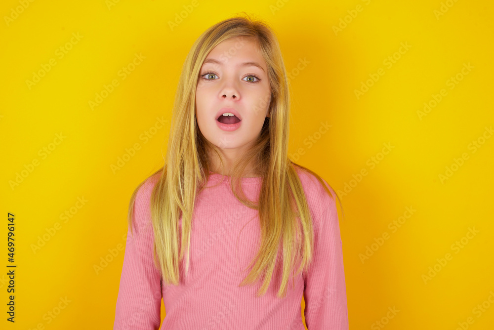 Shocked caucasian little kid girl wearing long sleeve shirt over yellow background stares bugged