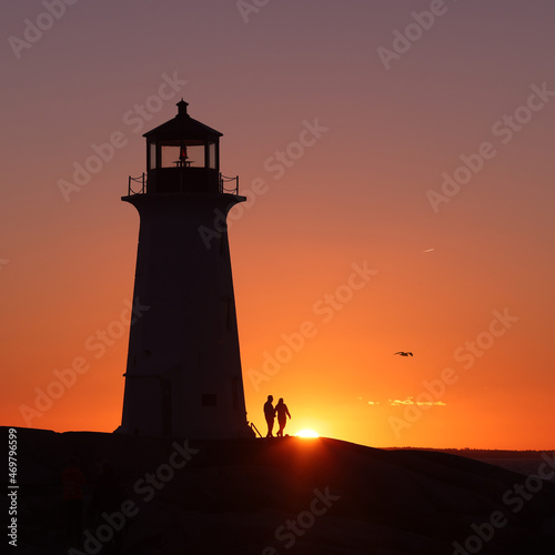 A couple holding their hands in the silhouette background of a lighthouse on a beautiful sunset full of red and orange sky. Valentine Peggy's Cove Lighthouse, Halifax, Nova Scotia, Canada