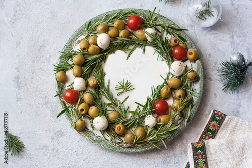 Christmas wreath on a mozzarella plate of cherry tomatoes and olives, decoration for the Christmas table on white background . photo