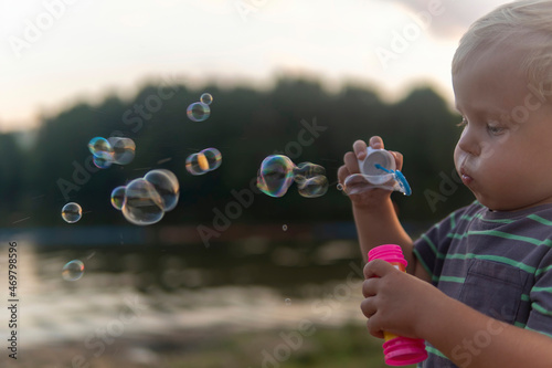 little boy blowing soap bubbles by the lake in the park