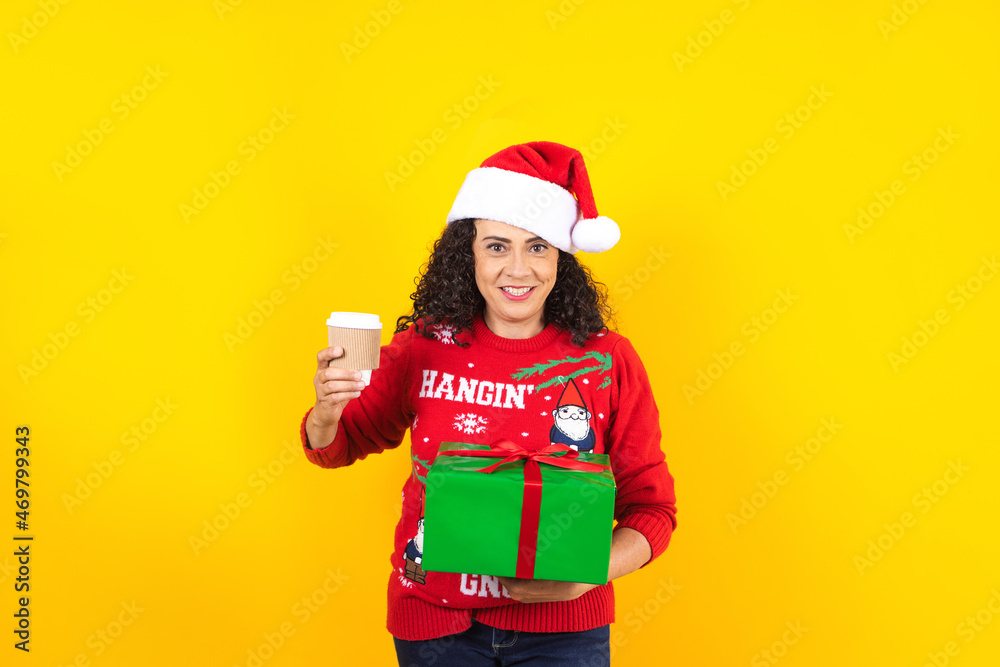 Portrait of Latin adult woman holding Christmas gift box on a yellow background in Mexico latin america	