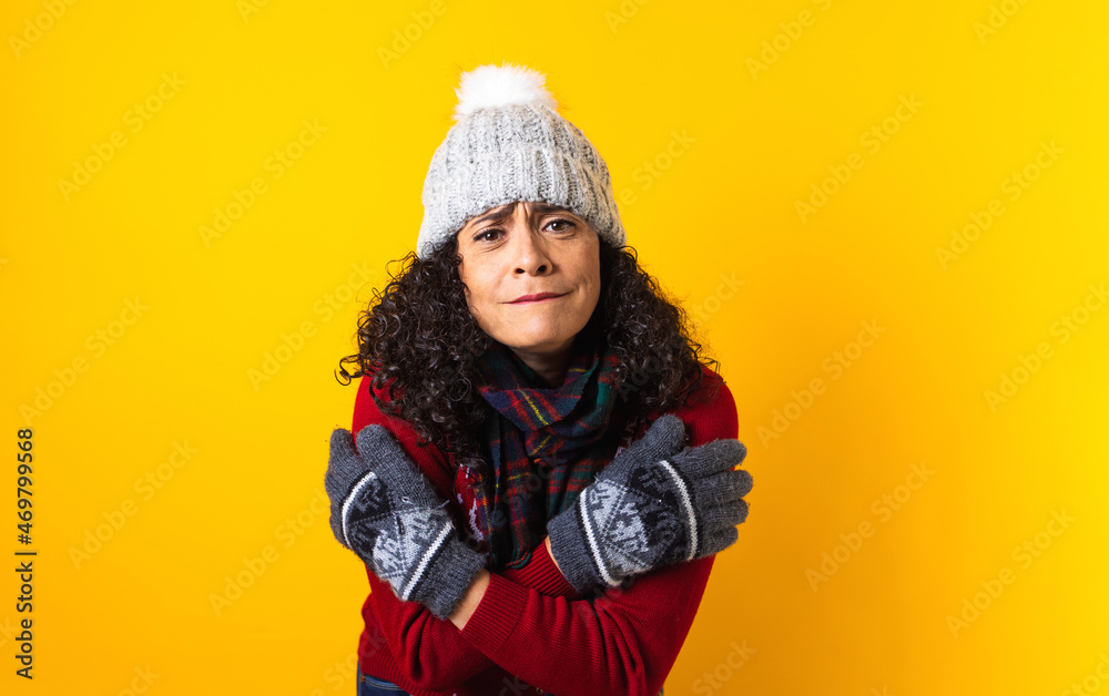 young latin woman with frozen face and cold in Santa hat Christmas sweater and warming up holding arms crossed on yellow background. Christmas and winter concept in Mexico Latin America young latin woman with frozen face and cold in Santa hat Christmas sweater and warming up holding arms crossed on yellow background. Christmas and winter concept in Mexico Latin America