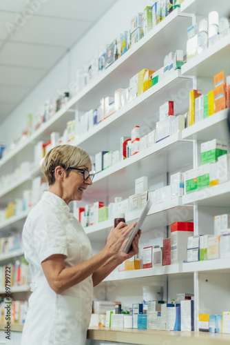 Beautiful senior female pharmacist checking medications on a shelf