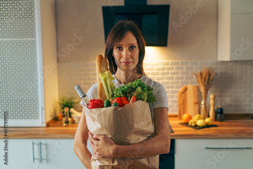Young woman returning home from shopping with paper bag with groceries.