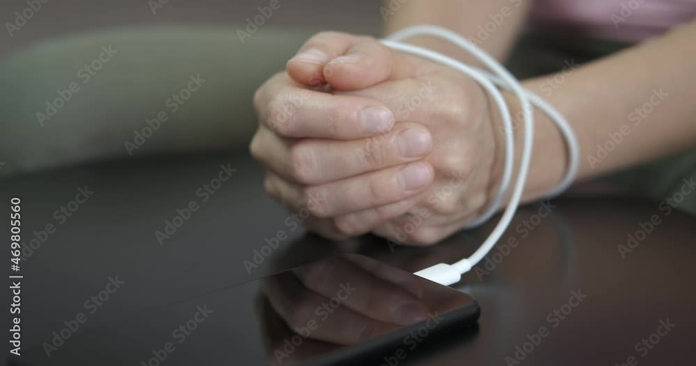 Using the mobile phones all time. A girl with tied hands stay by her mobile phone. A concept of internet and smart dependence. Using the mobile phones all time. A girl with tied hands stay by her mobile phone. A concept of internet and smart dependence.