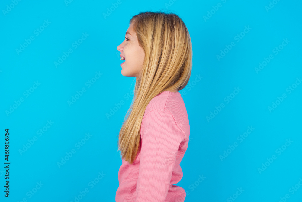 Profile portrait of nice caucasian little kid girl wearing long sleeve shirt over blue background look empty space toothy smile Profile portrait of nice caucasian little kid girl wearing long sleeve shirt over blue background look empty space toothy smile