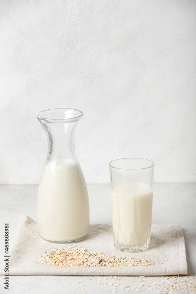 Alternative vegetable oat milk is poured into a bottle and glass cup, next to oatmeal on a white background. Healthy beverages healthy concept