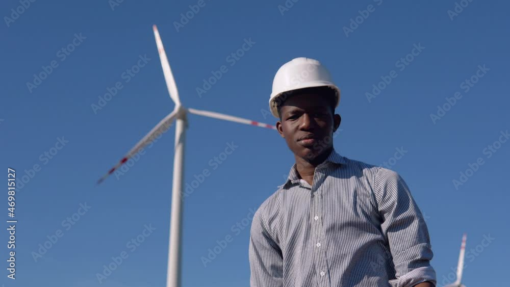 African American electrician engineer standing on the background of a windmill at an air power plant African American electrician engineer standing on the background of a windmill at an air power plant