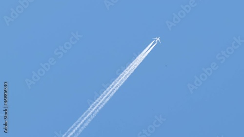 Distant passenger jet plane flying on high altitude on clear blue sky leaving white smoke trace of contrail behind. Air transportation concept