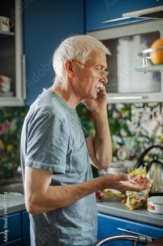 man with gray hair and a mustache speaks on cell phone in the kitchen in everyday life. elderly gray-haired man with a bald head is holding a phone and talking to his family