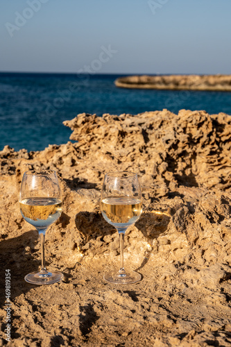 Two glasses of cold white dry white wine served on rocks in blue sea bay near Protaras touristic town on Cyprus