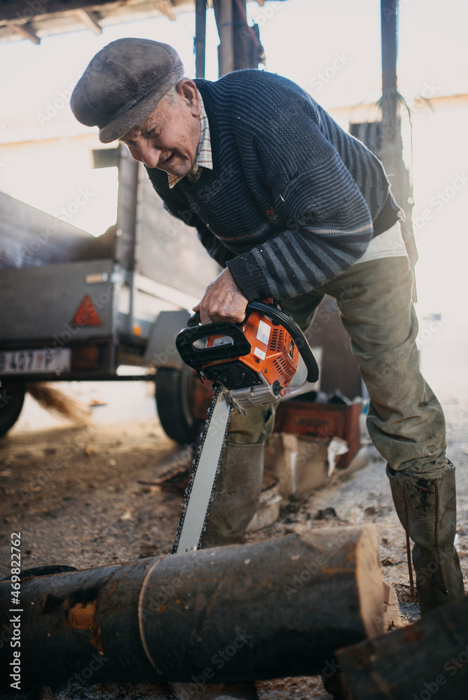 Old man smiling while cutting firewood with a chainsaw. Old man smiling while cutting firewood with a chainsaw.
