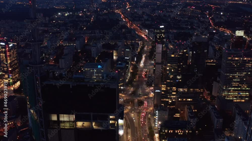 Forwards fly around skyscrapers, revealing busy streets below. Aerial view of cityscape at night. Warsaw, Poland