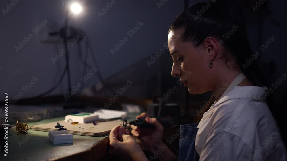 Side view skilled female silversmith polishing ring with manual tool in workshop with blue light. Confident concentrated professional Caucasian woman jeweller working indoors. Slow motion Side view skilled female silversmith polishing ring with manual tool in workshop with blue light. Confident concentrated professional Caucasian woman jeweller working indoors. Slow motion