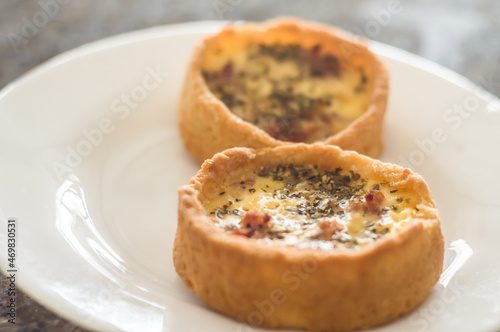 ham and cheese quiche with oregano on a white plate with selective focus