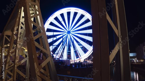 Timelapse of ferris wheel in Cologne near Schokoladenmuseum (Choclate museum). Spinning and stopping with long exposure. Old Bridge in goreground. Blue lights and a smooth camera movment. V2 photo