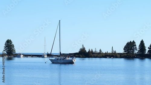 Calm marina water at Grand Marais, in northern Minnesota, with a moored sailboat on a sunny morning, and Gitchi-Gami or Lake Superior in the distance. Handheld clip with subtle zoom in. photo