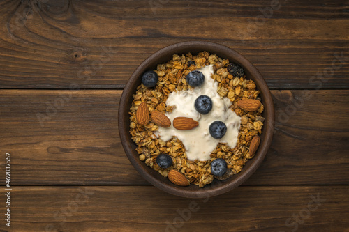 Muesli with yogurt in a deep clay bowl on a rustic table. Flat lay.