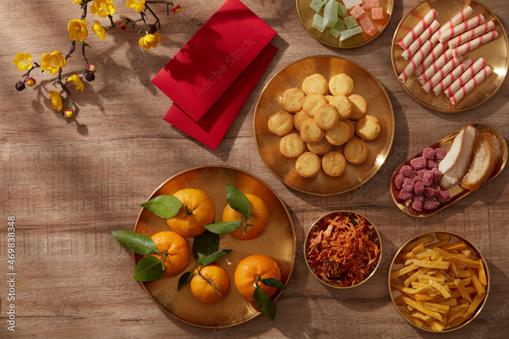 Happy lunar new year with mandarin orange teapot in golden dish candy jam , fried potato flower red pocket biscuit , wooden background photography Tet holiday content , chinese new year