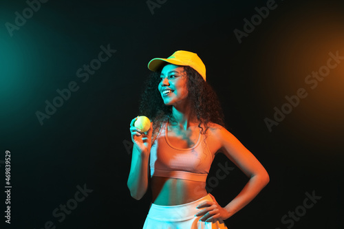 Beautiful African-American woman with tennis ball on dark background