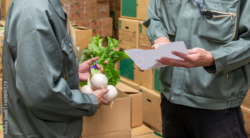 青果市場の倉庫で野菜を手に打ち合わせをする、作業着姿の2人の男性 photo