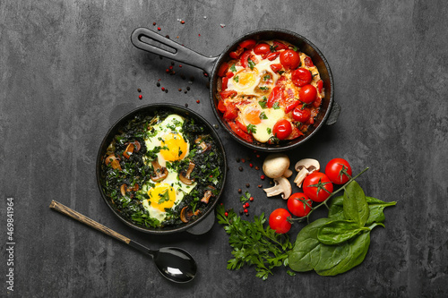 Frying pans with tasty Shakshouka and vegetables on black background